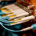 Equipamento de conexão óptica visto de cima, com diversos cabos e conectores dispostos em uma estrutura metálica