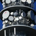 Torre de telecomunicações com várias antenas parabólicas contra o céu.
