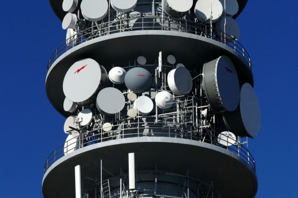 Torre de telecomunicações com várias antenas parabólicas contra o céu.