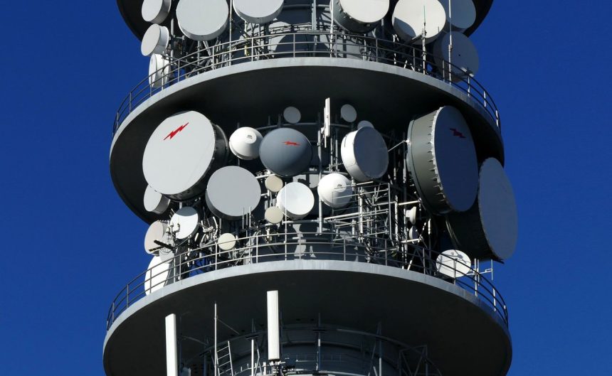 Torre de telecomunicações com várias antenas parabólicas contra o céu.